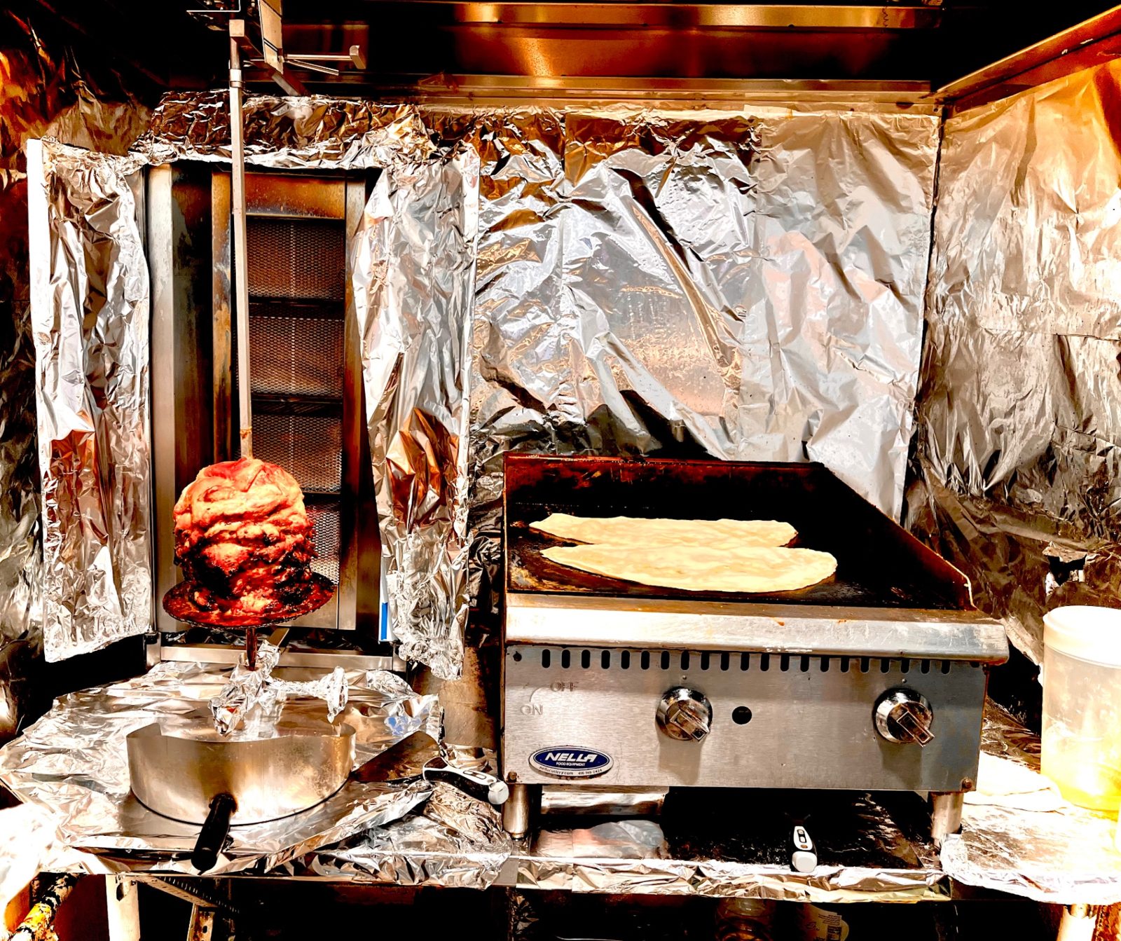 Chicken shawarma turning on the spit beside the flatbread grill
